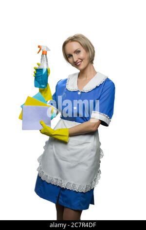 Blonde maid in yellow rubber gloves demonstrating cleaner spray and dusters on white background. Stock Photo