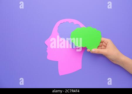 Female hand with paper brain and human head on color background. Neurology concept Stock Photo