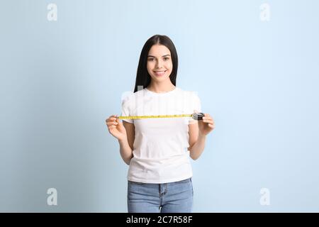 Young woman with measuring tape on color background Stock Photo