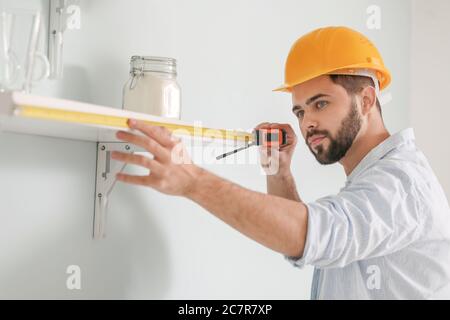 Young man taking measures of shelf at home Stock Photo