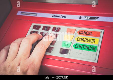 Closeup shot of fingers pressing buttons on a red Spanish ATM machine keypad Stock Photo