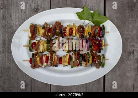 Skewer before grilling composed of bacon onions tomatoes meat pork zucchini peppers on a plate with leaves on a wooden table Stock Photo