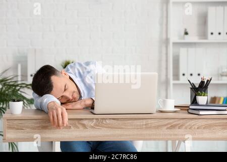 Young man falling asleep during work in office. Concept of sleep deprivation Stock Photo