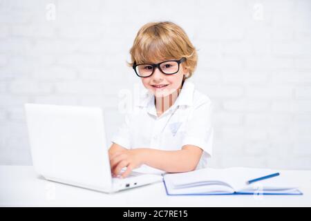 happy cute little school boy in glasses doing homework and using laptop at home Stock Photo