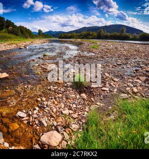 Mountain river stream of water in the rocks with blue sky. Clear river with rocks leads towards mountains lit by sunset. Carpathian region. Ukraine Stock Photo