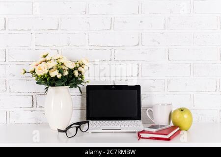 workplace with modern laptop on the table over white brick wall background Stock Photo