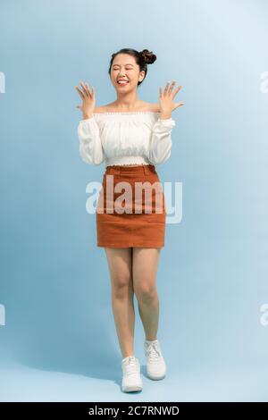 Charming girl with bun shrugging, spreading hands in clueless gesture, smiling broadly, being in good mood, Stock Photo