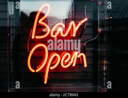 Illuminated neon orange [Bar Open] sign on a black striped background Stock Photo