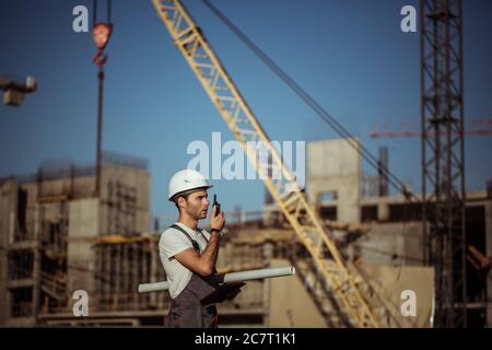 Engineer builder using tablet and walkie talkie, giving instructions at a construction site Stock Photo
