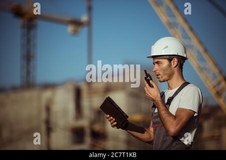 Engineer builder using tablet and walkie talkie, giving instructions at a construction site Stock Photo