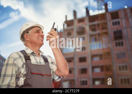 Senior engineer builder using a walkie talkie at a construction site. Sunset time Stock Photo