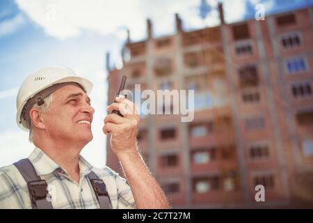 Senior engineer builder using a walkie talkie at a construction site. Sunset time Stock Photo