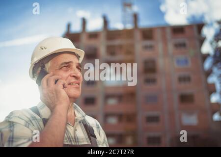 Senior engineer builder using a walkie talkie at a construction site. Sunset time Stock Photo