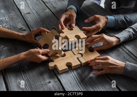 Business people team sitting around meeting table and assembling wooden jigsaw puzzle pieces unity cooperation ideas concept Stock Photo