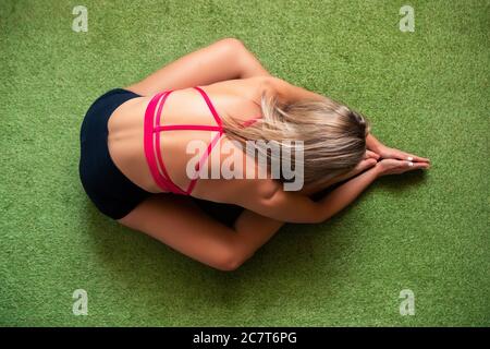 High angle view of a young female doing the Ardha Kurmasana pose on a carpet under the lights Stock Photo