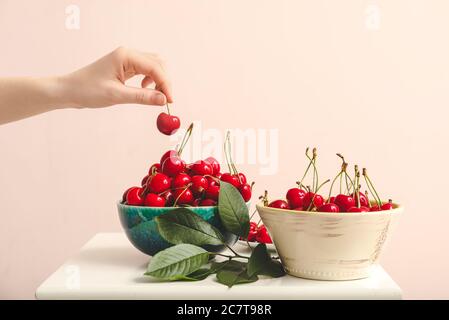 Female hand and bowls of sweet cherry on color background Stock Photo