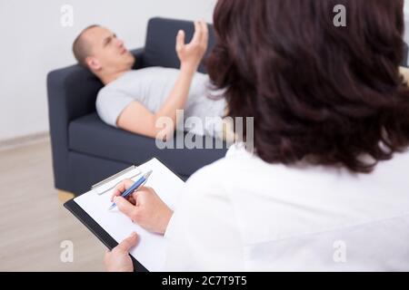 young man lying on sofa and talking about his problems with psychotherapist or psychologist Stock Photo