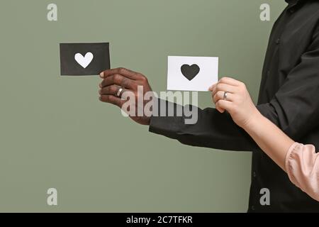 Hands of Caucasian woman and African-American man holding paper sheets with drawn heart on color background. Racism concept Stock Photo