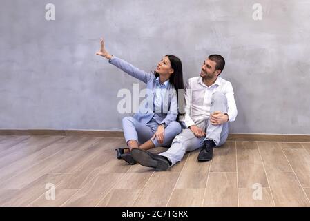 Excited young couple sitting on the floor of empty new apartment and planning arrangement Stock Photo