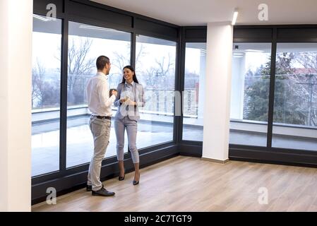 Young colleagues having a conversation during the coffee break while standing near the window Stock Photo