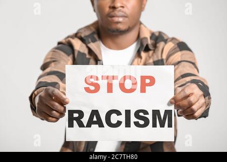 Sad African-American man with poster on light background. Stop racism Stock Photo