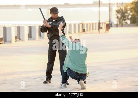 Aggressive African-American police officer mistreating man outdoors Stock Photo