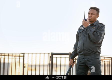 African-American police officer with two-way radio outdoors Stock Photo