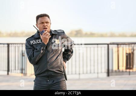 African-American police officer with two-way radio outdoors Stock Photo