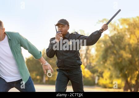 Aggressive African-American police officer mistreating man outdoors Stock Photo