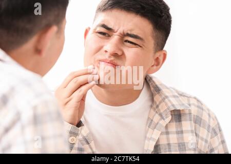 Asian man with cold sore looking on his reflection in mirror Stock Photo