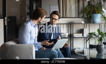 Caucasian male colleagues discuss ideas working on laptop Stock Photo
