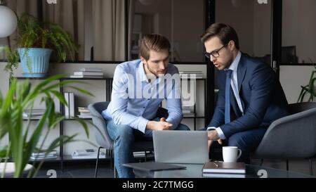 Serious businessmen look at laptop screen discussing project together Stock Photo