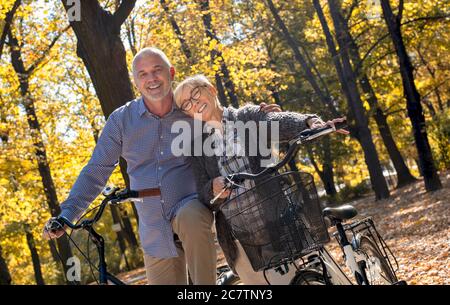 Happy elderly couple riding a bicycle in the park in the autumn Stock Photo