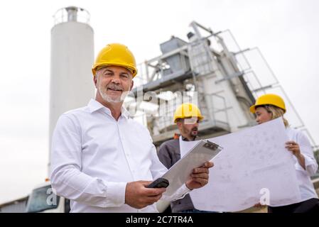 Senior engineer smiling with his colleagues in the background at a construction site Stock Photo