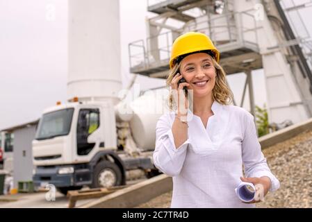 Portrait of a caucasian woman wearing yellow hard hat  on phone and smiling at construction site Stock Photo