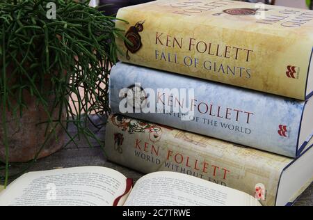 Viersen. Germany - July 9. 2020: View on wood table with open book, stack of Ken Follett novels books and green plant Stock Photo