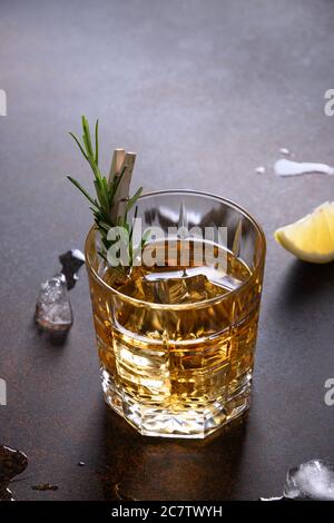 One shot of whiskey with rosemary on dark brown. Vertical orientation. Stock Photo