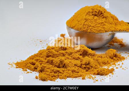 A metal measuring spoon piled with turmeric with some turmeric spilled on an isolated white background Stock Photo