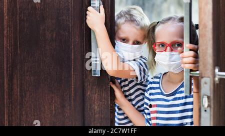 Little children looking unhappy and depressed after staying at home due banned street activity. Kids wearing medical face masks go out Stock Photo