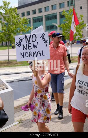 Ottawa, Canada. July 19th, 2020. Young girl wearing face mask on eyes with sign 'No New Normal' part of crowd of about one hundred walked from City Hall to the Canadian Parliament protesting current city bylaws requiring masks to be worn inside all public places in the city. The crowd also use to occasion to show their displeasure towards all level of government related to the imposed guidelines during the Pandemic which has to date killed more than 8800 people across the country. Credit: JF Pelletier/Alamy Live News Stock Photo