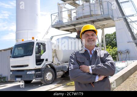 Happy male construction worker standing with folded arms with a truck on the background Stock Photo