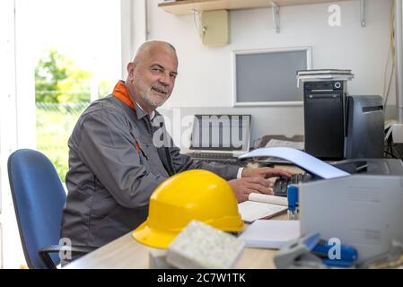 Male construction worker using the computer on the desk under the sunlight through the windows Stock Photo
