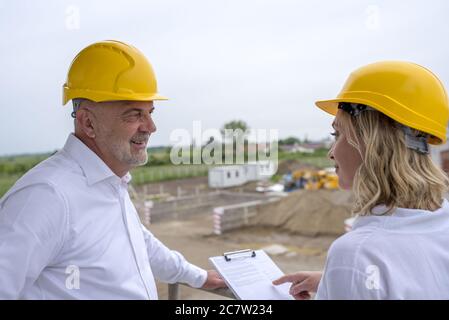 Construction workers with yellow helmets discussing documents under a cloudy sky at daytime Stock Photo