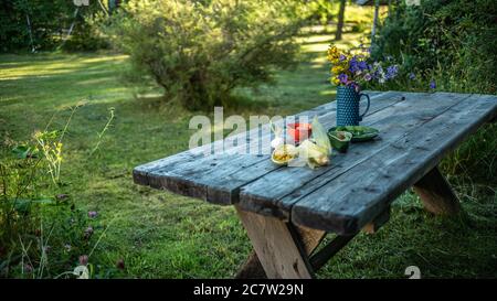 Garden with wooden table of old planks in the country with flowers and preparation with vegetables on a nice summer day in Sweden Stock Photo