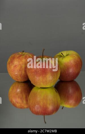 Three red apples on mirroring table on mirror gray background with reflection isolated close up Stock Photo