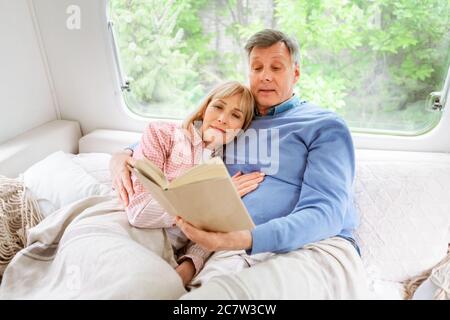 Family bedtime reading. Loving mature husband and wife with book lying in bed at trailer Stock Photo