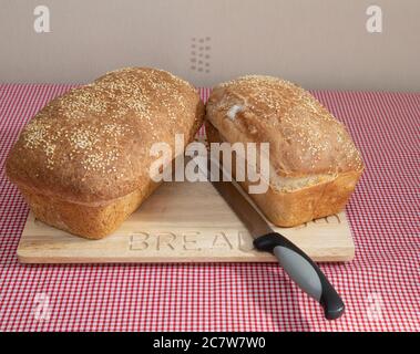 Two loaves of Freshly baked loaf of bread with sesame seeds on a wooden bread board Stock Photo