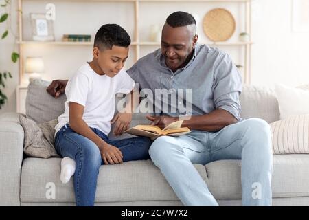 Pastime With Grandpa. Senior African Man Reading Book With Grandson At Home Stock Photo