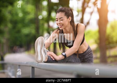 Flexible Asian Girl Stretching Leg Muscles While Working Out In City Park Stock Photo