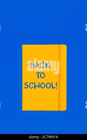 Back to school handwritten sign on yellow leather cover notebook over blue paper background with copy space Stock Photo
